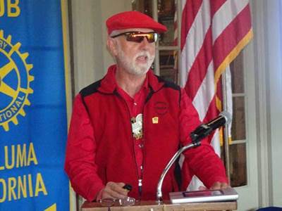 A person in red jacket and hat standing at a podium

Description automatically generated