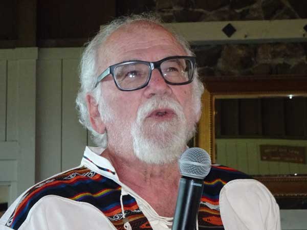 A person with glasses and a white beard speaking into a microphone

Description automatically generated