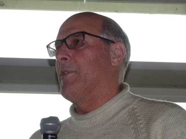 A person wearing glasses and a sweater speaking into a microphone

Description automatically generated