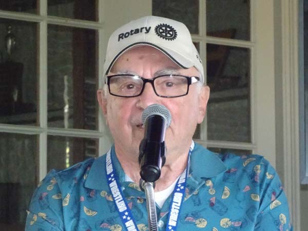 A person wearing a hat and glasses speaking into a microphone

Description automatically generated