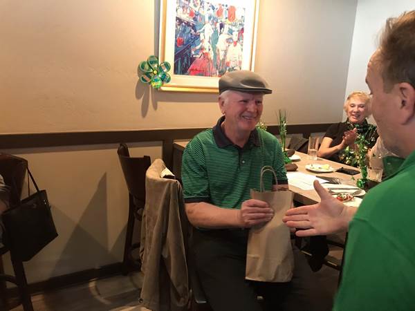 A person in a green shirt and hat holding a brown bag

Description automatically generated