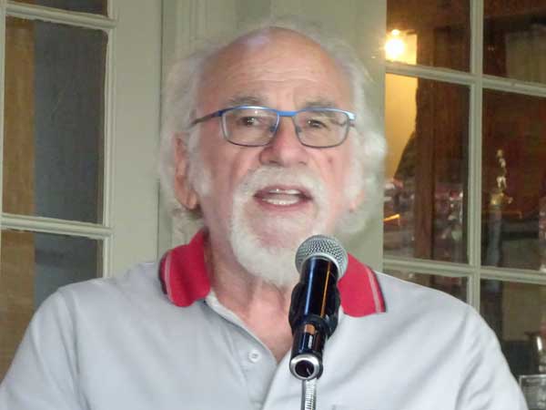 A person with a white beard speaking into a microphone

Description automatically generated