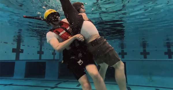 A person in a life vest holding a person in a pool

Description automatically generated