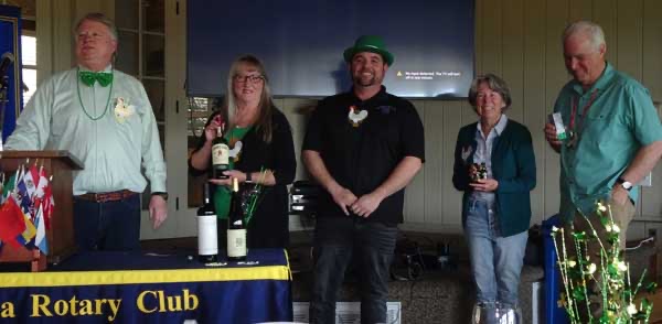 A group of people standing next to a table with bottles of wine

Description automatically generated